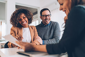 Couple smiling and talking to a third person as all look at a sheet of paper