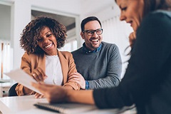 Couple smiling and talking to a third person as all look at a sheet of paper