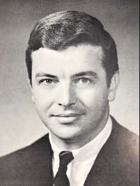 Black and white photo of person with short, coifed hair wearing a suit and tie.