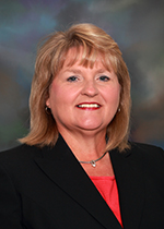 Smiling person with shoulder length blond hair and bangs, wearing a red shirt and black suit jacket