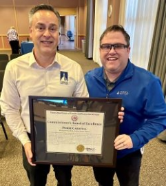 Two people smiling holding a framed award