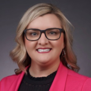 Kati Buchanan waring pink blazer, black shirt and black square frame glasses