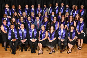 Large group of people sitting in formal attire wearing purple graduation stoles