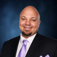 Smiling person with facial hair in a business suit wearing a green tie and pocket square