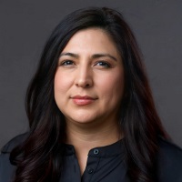 Person with long dark hair gently curled wearing lip gloss and a black mock collar shirt.