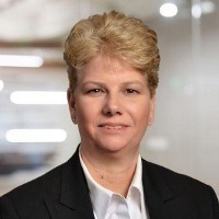 Smiling person with short blond hair curled and styled voluminously wearing a white button up under a black blazer