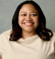 Smiling person with shoulder length, gently curled brown hair wearing a cream top and red lipstick
