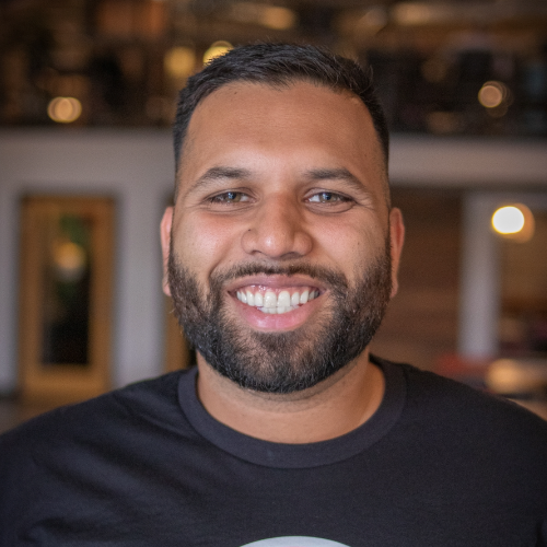 Smiling person with short dark hair pushed to the side and a close cropped beard.