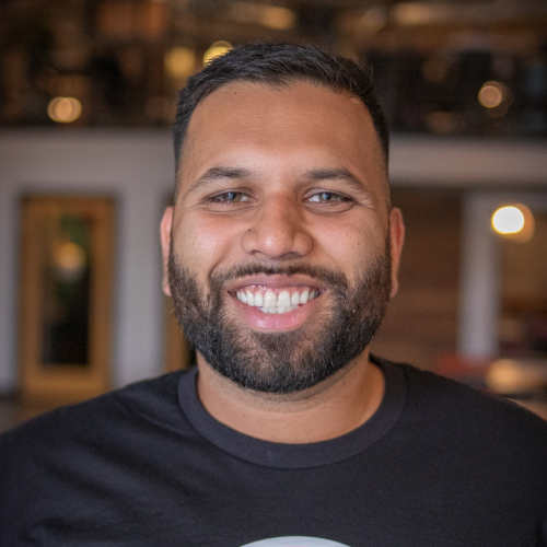 Smiling person with short dark hair pushed to the side and a close cropped beard. 