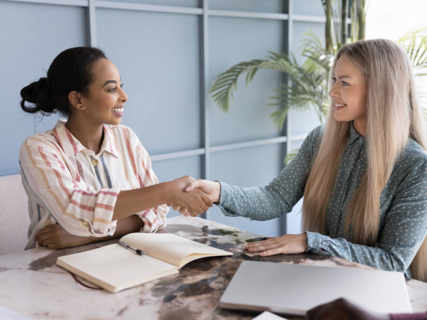 Two women sitting at a table shaking hands