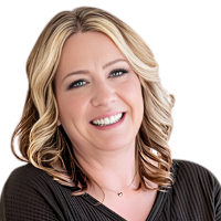 Smiling person with curled blond hair just past the shoulders wearing a black top and a small necklace