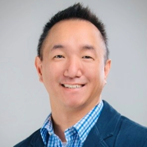 Smiling person with short, faux hawk dark hair wearing a blue checkered shirt with a blue blazer