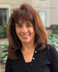 Smiling person with shoulder length brown hair and bangs wearing a black shirt and red lipstick.