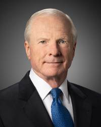 Distinguished person with short white hair neatly brushed to the side wearing a black suit, white shirt and blue tie.