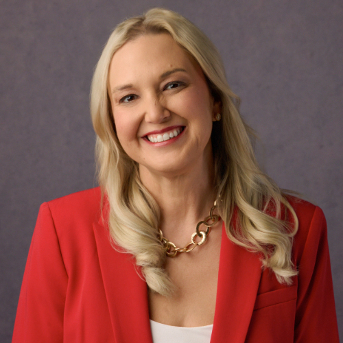 Smiling person with long curly brown wearing a pink blazer over a black shirt