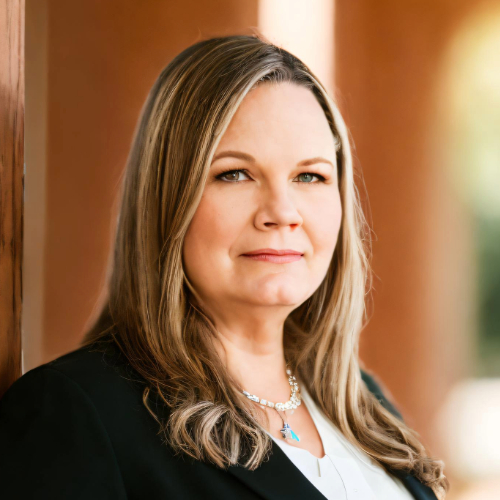 Person with long blond hair past shoulders wearing blazer, white blouse and statement necklace