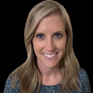 Smiling person with long blond hair gently curled wearing a speckled gray top