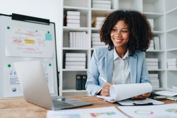 Smiling person taking notes and looking at a laptop.