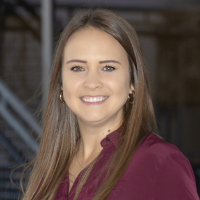 Smiling person with long straight brown hair wearing a maroon blouse