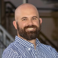 Smiling person with brown facial hair wearing a blue and white checked shirt