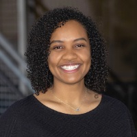 Smiling person with shoulder length tightly curled black hair