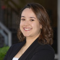 Smiling person with shoulder length brown hair wearing a black blazer over a white shirt