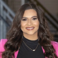 Smiling person with long curly brown wearing a pink blazer over a black shirt