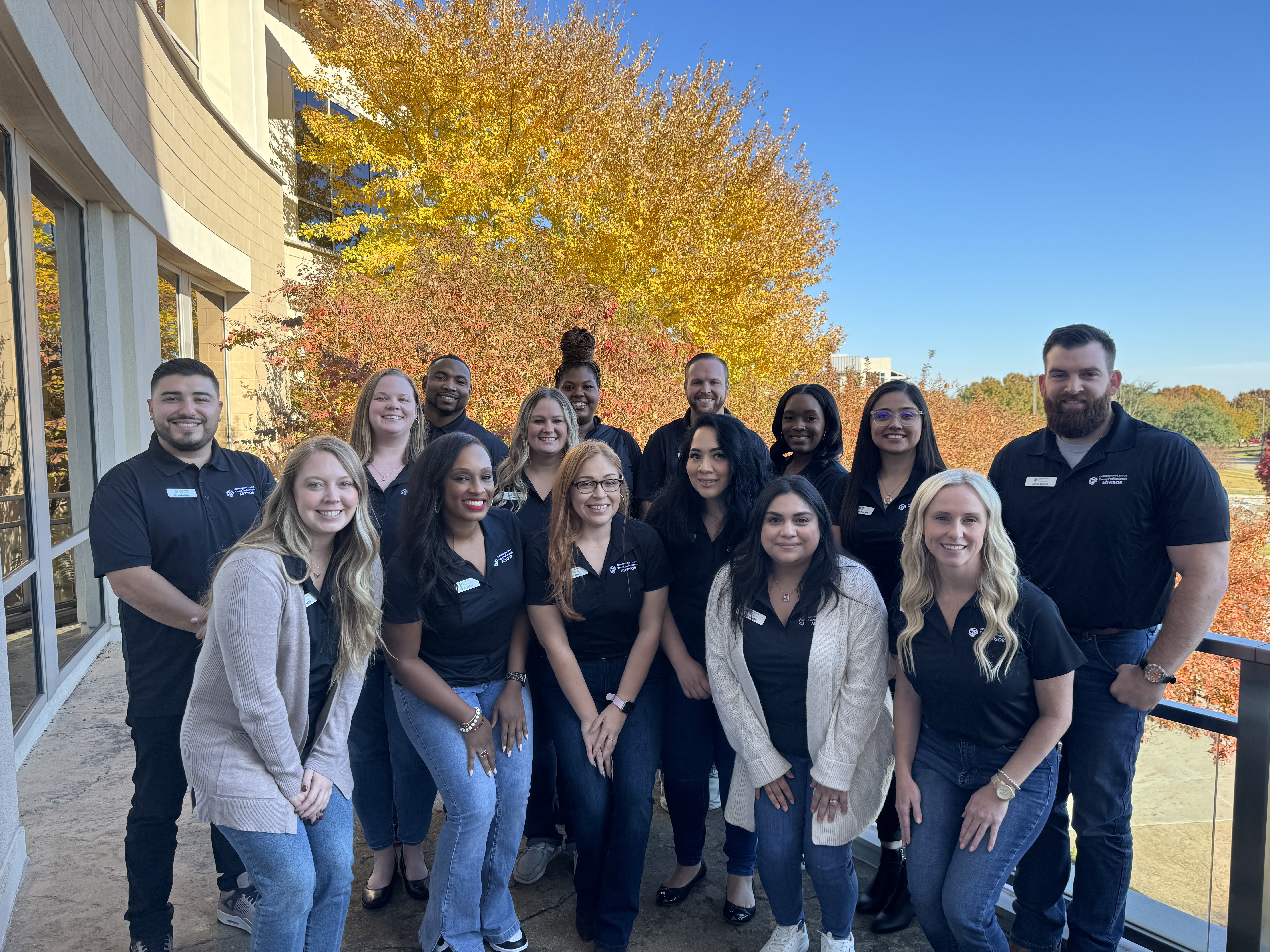 Group of fifteen people outside on a patio wearing black polos and jeans