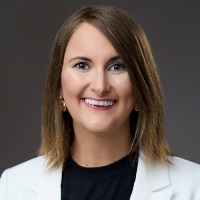 Smiling person with shoulder length brown hair wearing a black sweater and a delicate necklace