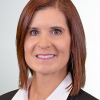 Smiling person with an auburn bob, pink lipstick and wearing professional attire